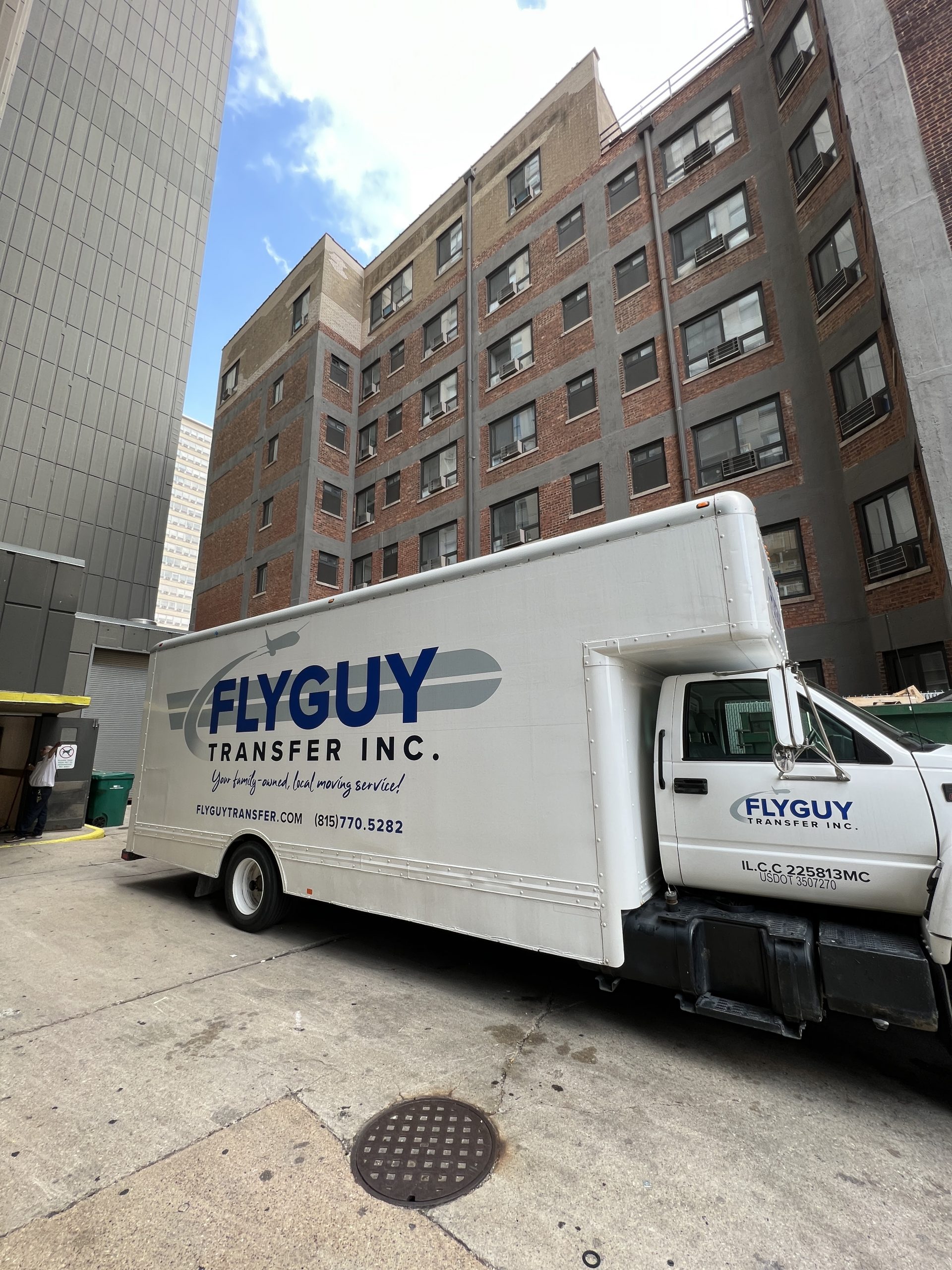 Fly Guy Tranfer moving truck parked outside multi-story building. Fly Guy Transfer